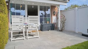 A patio with a white metal table and chairs, a grey outdoor storage unit, and a white fence. - Möwenstraße Haus 1 Inkl. Wlan (Grömitz)