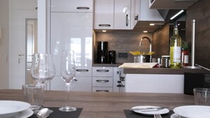 Una cocina moderna con armarios blancos, encimera de madera y un comedor dispuesto con platos, cubiertos y copas de vino.