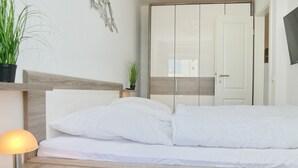 Una cama bien hecha con sábanas blancas, una lámpara de noche y una pequeña planta en maceta sobre la mesita.