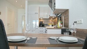 Una cocina moderna con armarios blancos, encimera de madera y horno integrado. Hay copas de vino y platos sobre la mesa, y una cafetera en la encimera.
