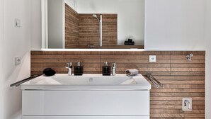 Ein modernes Badezimmer mit einem großen Spiegel, Holzvertäfelung, einem weißen Waschbecken mit zwei Wasserhähnen und einem Handtuchhalter.