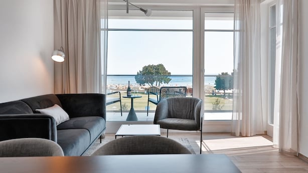 Ein modernes Wohnzimmer mit einem großen Fenster, das Meerblick und einen Baum zeigt.