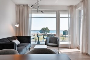Un salon moderne doté d’une grande fenêtre donnant sur la mer et un arbre.