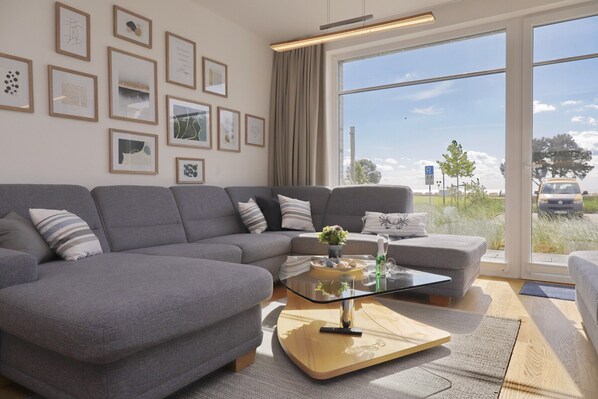 A modern living room with a grey sectional sofa, a glass coffee table, and framed artwork on the wall.