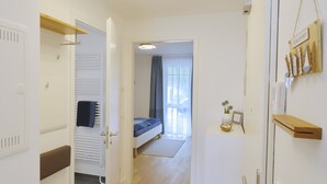 A hotel room with a bed, a bedside table, a radiator, a wooden shelf, and a door with a towel hanging on it. - Sealoft THE ONE Inkl. Wlan (Grömitz)