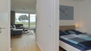 A modern bedroom with a large bed, a view of the outdoors, and a seating area with a sofa and coffee table. - Sealoft THE ONE Inkl. Wlan (Grömitz)