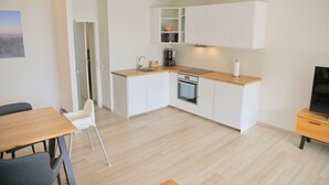 A modern kitchen with white cabinets, a wooden countertop, and a built-in oven. There is a dining area with a table and chairs, and a TV on a stand. - Miramar App. 617 Inkl. Wlan (Grömitz)