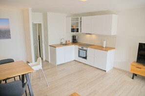 Eine moderne Küche mit weißen Schränken, einer Holz Arbeitsplatte und einem eingebauten Backofen. Es gibt einen Essbereich mit Tisch und Stühlen, sowie einen Fernseher auf einem Schrank.