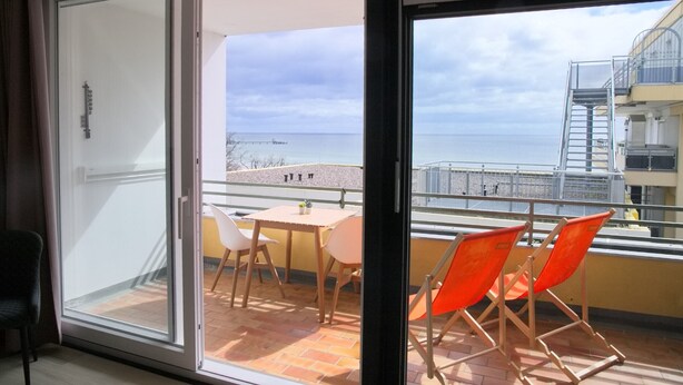 A balcony with a table and chairs, a view of the sea, and a building in the background. - Miramar App. 617 Inkl. Wlan (Grömitz)