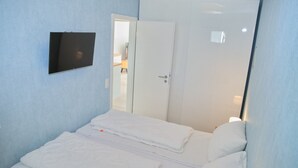 A bedroom with a bed, a TV mounted on the wall, and a door leading to another room. - Miramar App. 617 Inkl. Wlan (Grömitz)