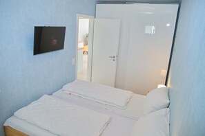 Ein Schlafzimmer mit einem Bett, einem an der Wand befestigten Fernseher und einer Tür zu einem anderen Raum.