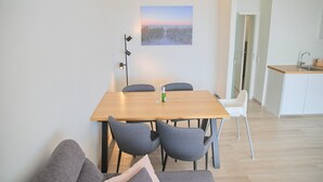 A modern living room with a wooden dining table, grey upholstered chairs, a grey sofa, and a painting of a sunset on the wall. - Miramar App. 617 Inkl. Wlan (Grömitz)
