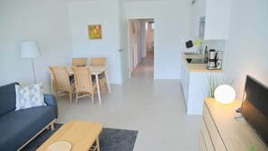 En moderne stue med sofa, sofabord og spiseplads. Et køkken med komfur og kaffemaskine kan ses i baggrunden.