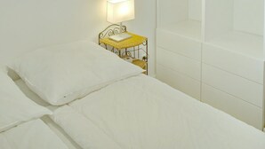 Et soveværelse med seng, natbord med lampe, hængende loftlampe og et garderobeskab med hylder og plads til ophængning.