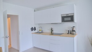 Et moderne køkken med hvide skabe, en træbordplade, en stålvask, en mikrobølgeovn og en kaffemaskine.