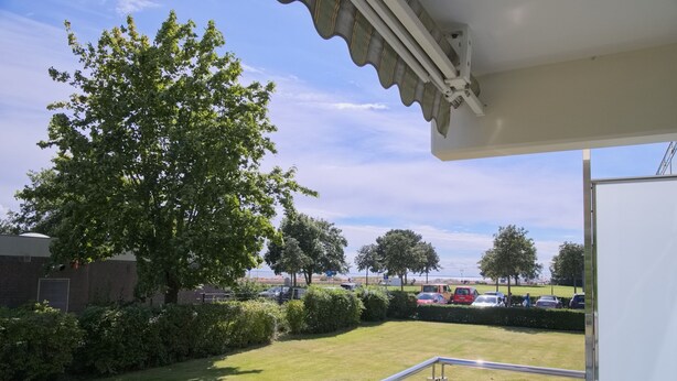 Balkon med udsigt over græs, træer og parkerede biler.