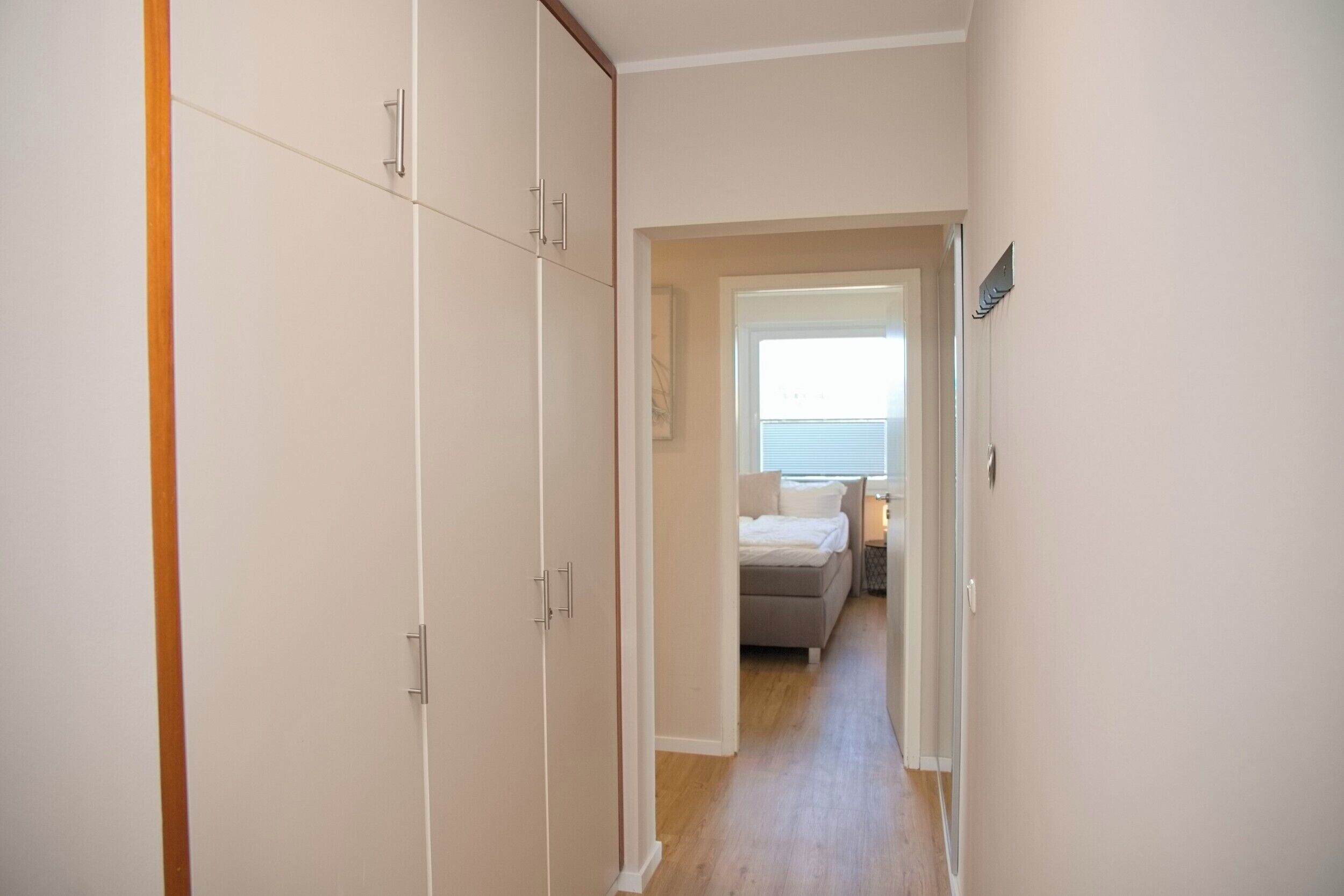 A hallway leading to a bedroom with a bed, a nightstand, and a window with blinds.