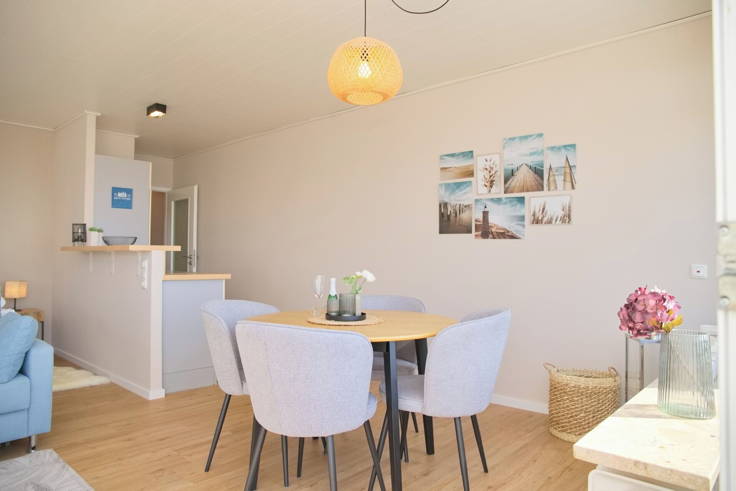 Een moderne eetruimte met een ronde tafel, vier grijze stoelen, een hanglamp en een wand met ingelijste foto’s.