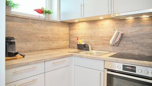 A modern kitchen with white cabinets, a built-in oven, and a window with plants. - Tannenburg 505 Inkl. Wlan (Grömitz)