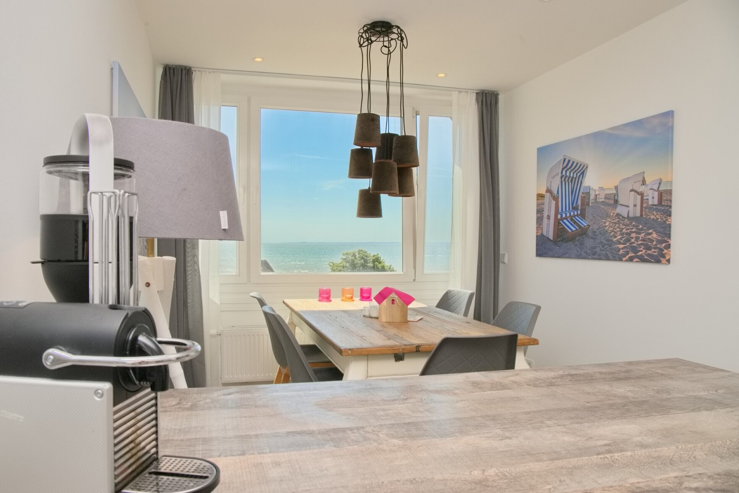 A dining area with a wooden table, chairs, a modern lamp, and a view of the sea through large windows.