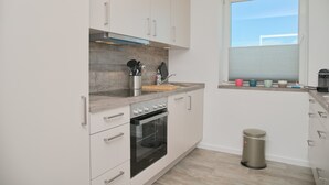 A modern kitchen with white cabinets, a built-in oven, and a window with blinds. - Tannenburg App. 508 Inkl. Wlan (Grömitz)
