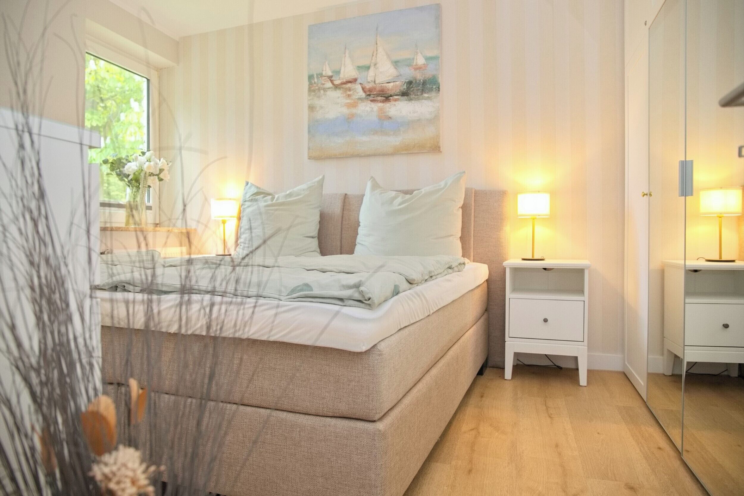 A bedroom with a bed, bedside tables, a nightstand, a mirror, and a painting on the wall.