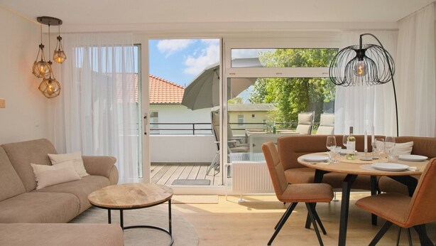 Una sala de estar moderna con un sofá, una mesa de centro y un comedor con sillas y una mesa preparada para una comida.