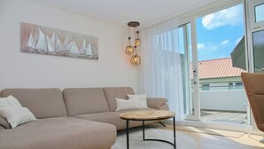 Una sala de estar moderna con un sofá color beige, una mesita de madera y un cuadro de veleros en la pared.