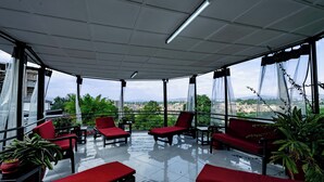 A covered outdoor seating area with red chairs and tables, large windows, and potted plants. - Blue Veil Villa (Kigali)