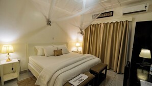 A hotel room with a bed, bedside tables with lamps, a bench, a curtain, and an air conditioning unit. - Blue Veil Villa (Kigali)
