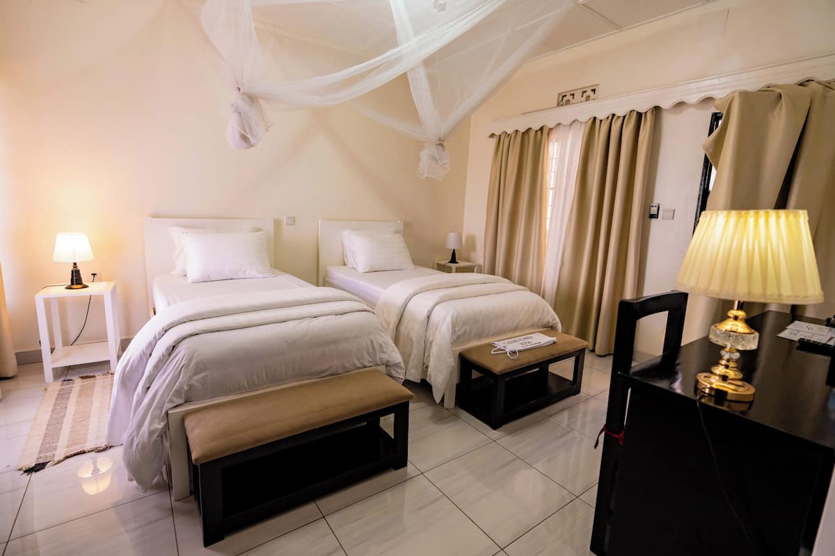 Une chambre d’hôtel avec deux lits, des tables de chevet, un banc, un bureau avec une lampe et un lit à baldaquin.