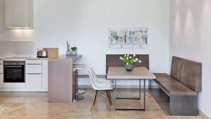 A modern kitchen with a built-in oven, a dining area with a bench and table, and a painting on the wall. - Linde Villa am Wörthersee mit Privatem Strand (Maria Wörth)