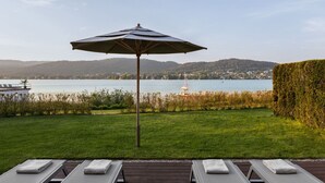 A pool area with lounge chairs and an umbrella, overlooking a lake with a sailboat and hills in the background. - Linde Villa am Wörthersee mit Privatem Strand (Maria Wörth)