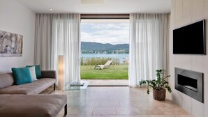 A modern living room with a sofa, a glass coffee table, and a TV mounted on the wall. - Linde Villa am Wörthersee mit Privatem Strand (Maria Wörth)