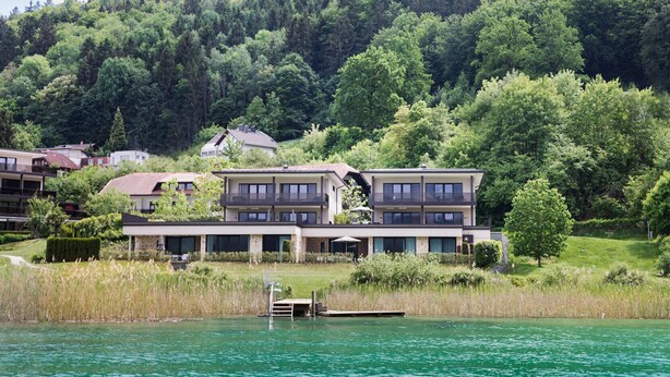 A lakeside hotel with a two-story building, a dock, and a forested hillside in the background. - Linde Villa am Wörthersee mit Privatem Strand (Maria Wörth)
