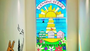 A colorful stained glass window with the text "Glen'sing Lodge" and "St Leonards on Sea" depicting a coastal scene with a lighthouse, beach houses, and flowers. - Gensing Lodge A Beautiful 3 Bedroom Boutique. Award Winning!  (Saint Leonards)