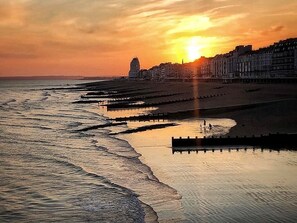 Sonnenuntergang an der Küste mit Strand, einer Pier und Gebäuden im Hintergrund.