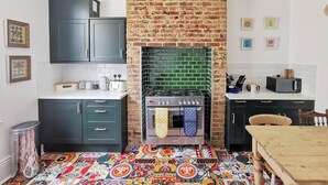 A kitchen with dark cabinets, a brick wall, a green-tiled backsplash, a gas stove, and a microwave. - Gensing Lodge A Beautiful 3 Bedroom Boutique. Award Winning!  (Saint Leonards)