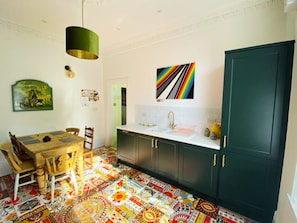 Een keuken met een vloer in een kleurrijk patroon, een eettafel met stoelen, een groen kastje en een hanglamp.