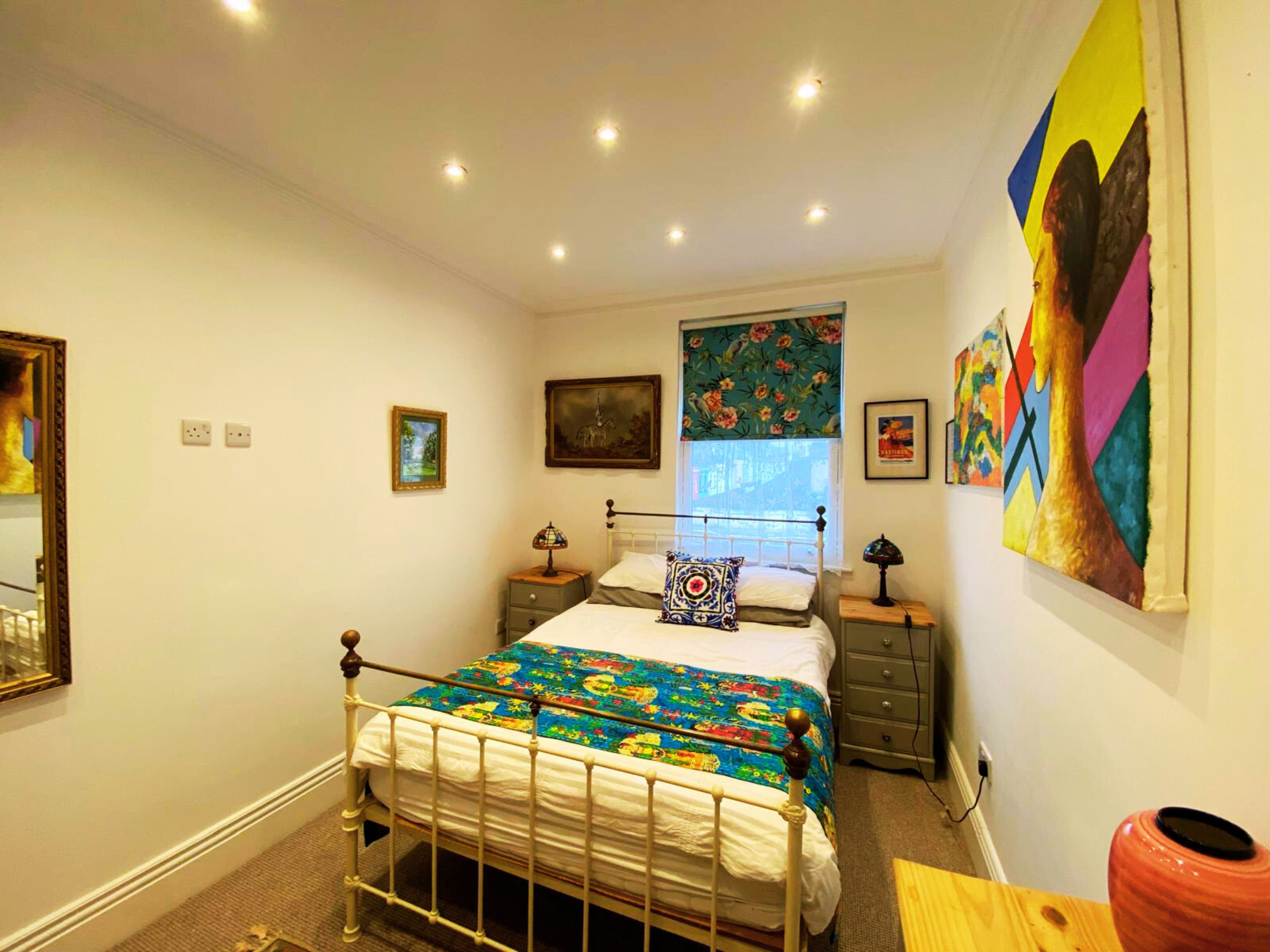 Een slaapkamer met een bed, nachtkastjes, een spiegel en kunstwerken aan de muur.