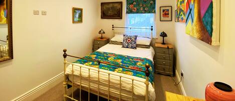 Een slaapkamer met een bed, nachtkastjes, een spiegel en kunstwerken aan de muur.