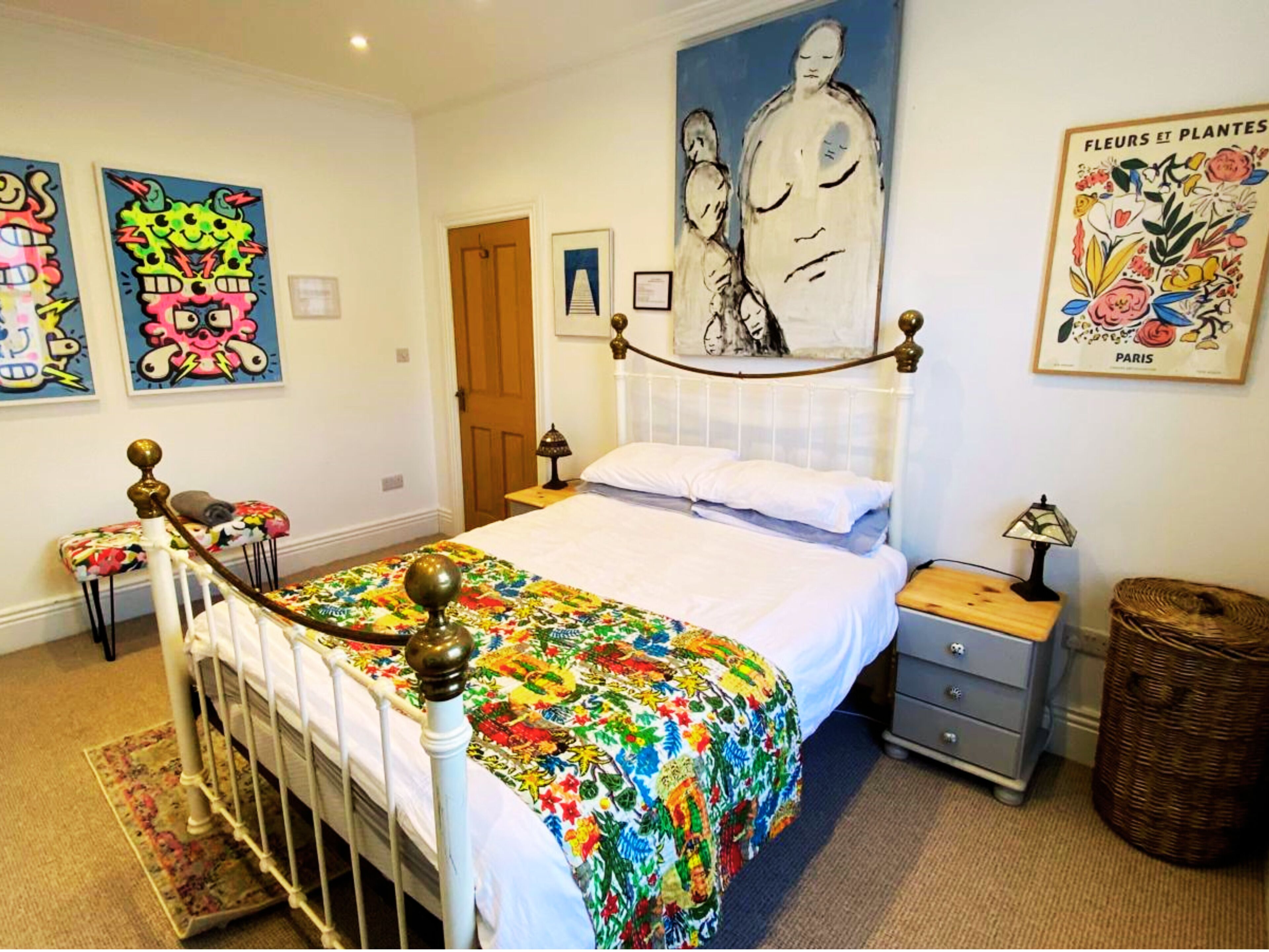 Une chambre à coucher comprenant un lit, une table de chevet, une lampe, une chaise, une porte et des œuvres d’art mural.