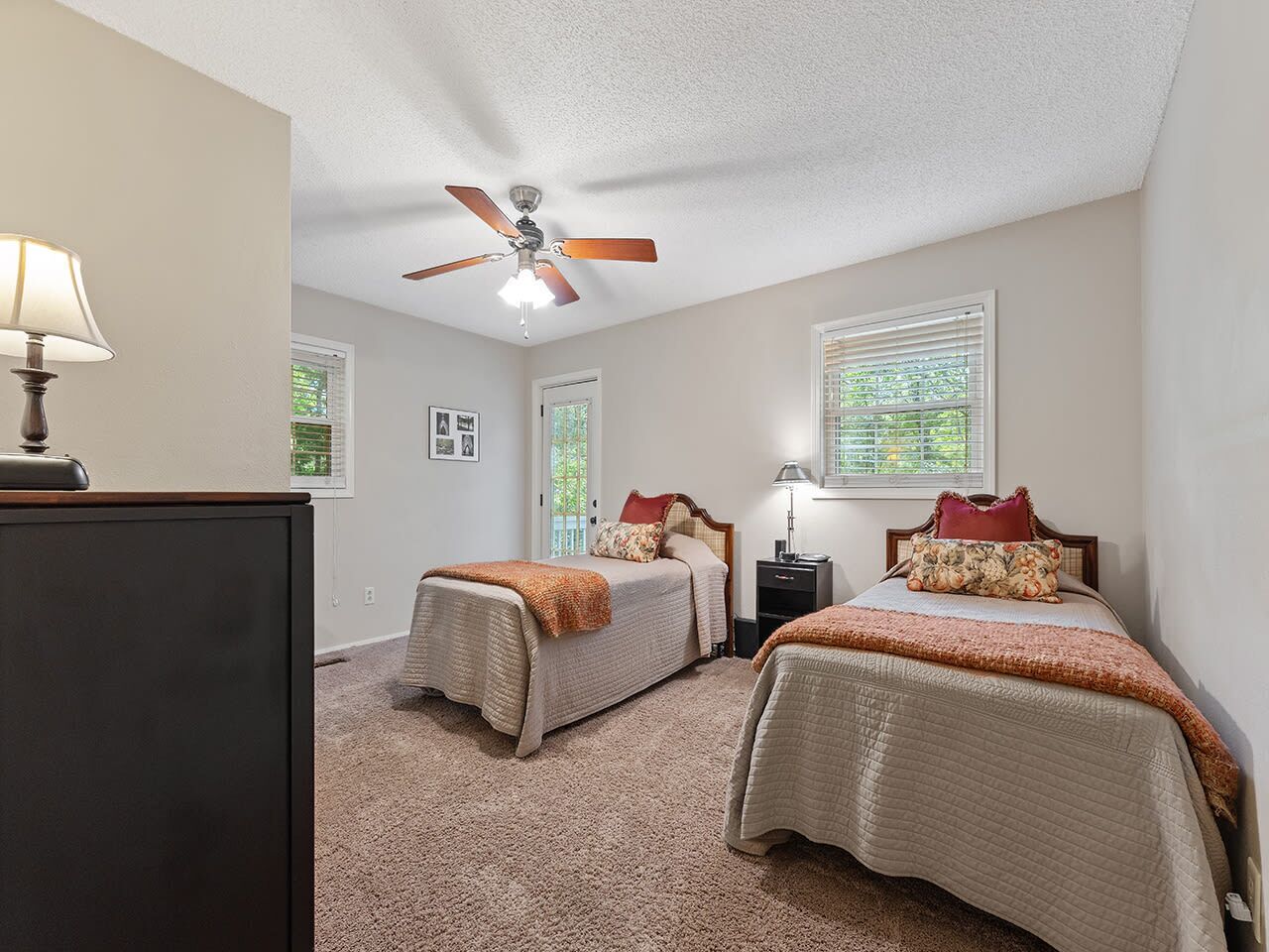 A bedroom with two beds, a ceiling fan, a nightstand with a lamp, and a dresser.