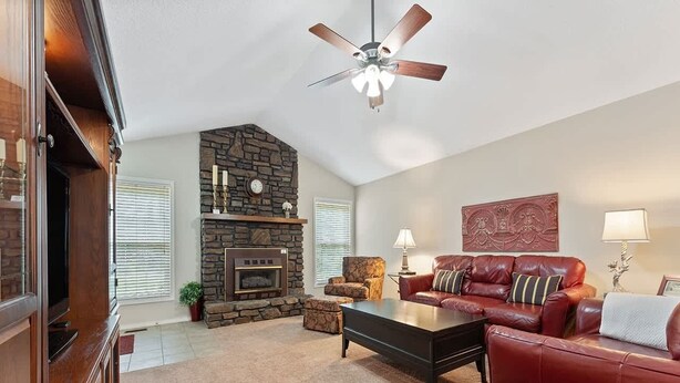 A living room with a stone fireplace, leather sofa, a coffee table, and a ceiling fan. - Blue on Basildon (Bella Vista)