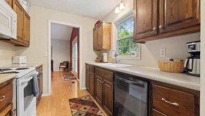 A kitchen with wooden cabinets, a dishwasher, a stove, and a coffee maker. - Blue on Basildon (Bella Vista)