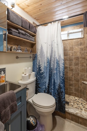 Ein Badezimmer mit Toilette, Ablagefläche mit Handtüchern und einer Duschvorhang mit Waldmusterung.