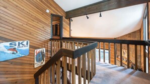 Eine Holztreppe mit Handlauf, eine Holzwand mit einem Skiaffiche und Blick auf einen Raum mit einer Steinwand.