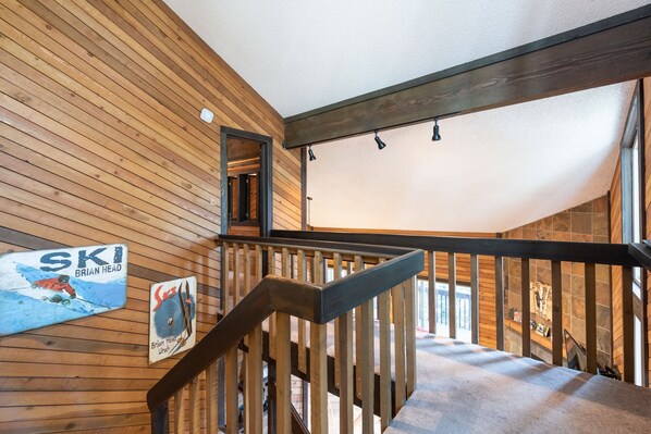 Eine Holztreppe mit Handlauf, eine Holzwand mit einem Skiaffiche und Blick auf einen Raum mit einer Steinwand.