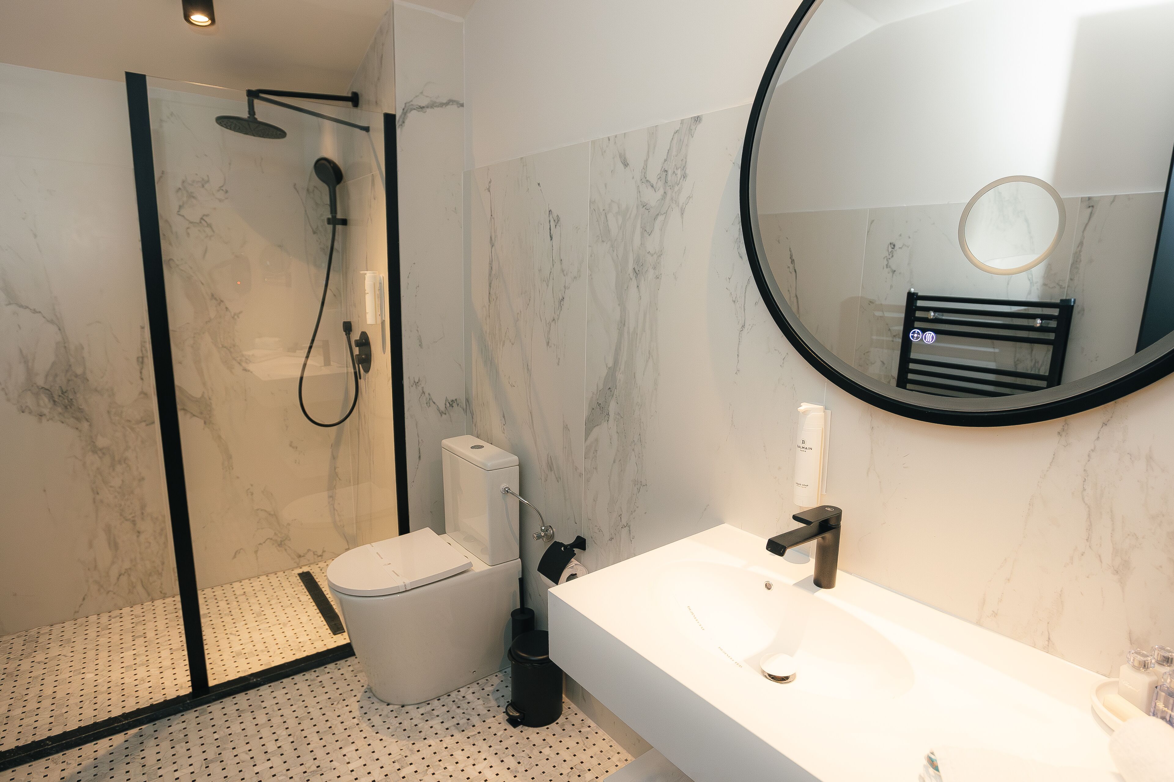 A modern bathroom with a glass-enclosed shower, a toilet, and a sink with a mirror above.