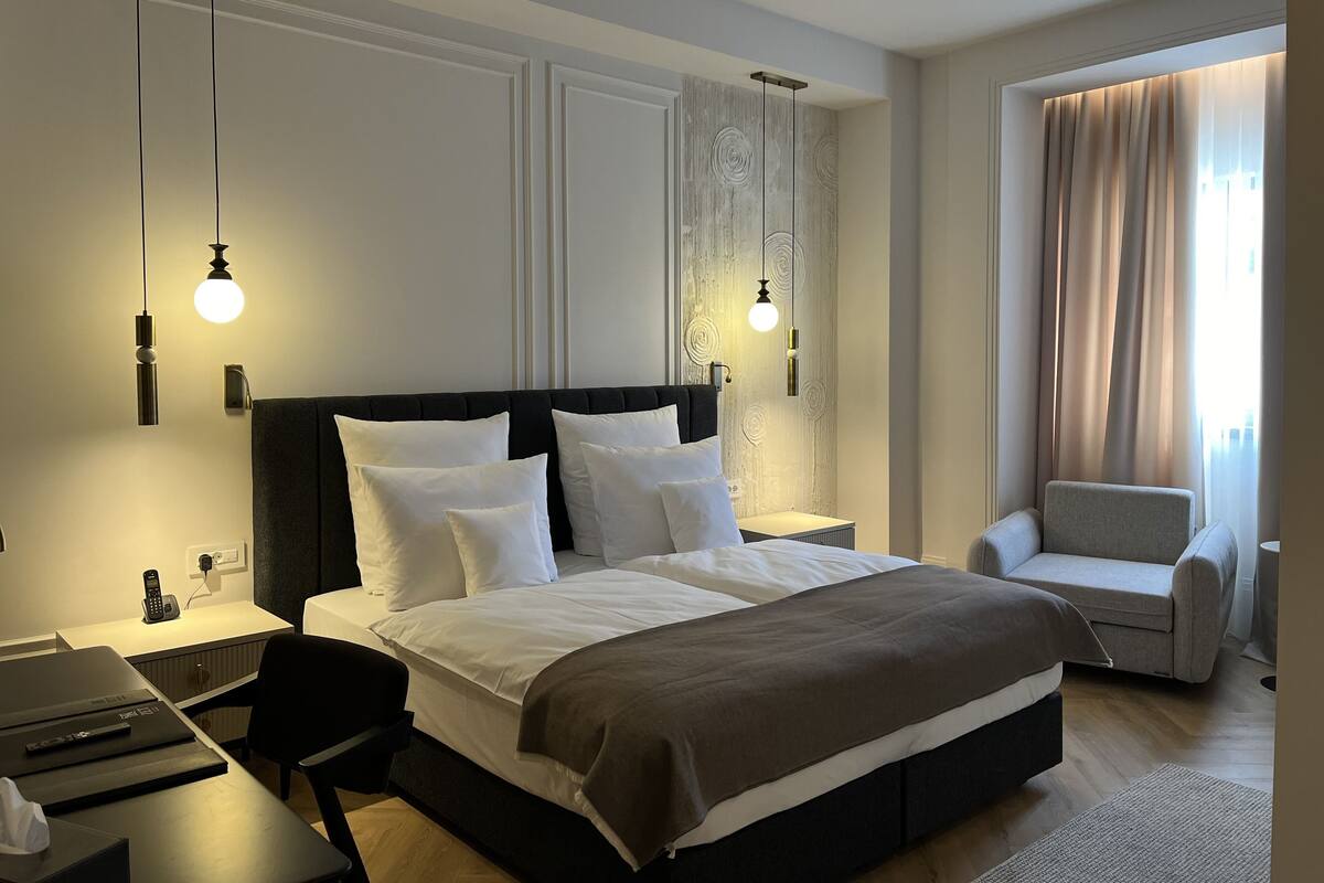 A modern hotel room with a large bed, bedside tables, a desk, and a chair.